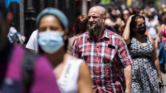 Un hombre pasea sin mascarilla rodeado por gente con mascarilla durante la COVID-19