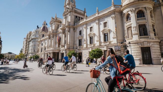 Un grup de turistes recorre la plaça de l'Ajuntament de València en bicicleta